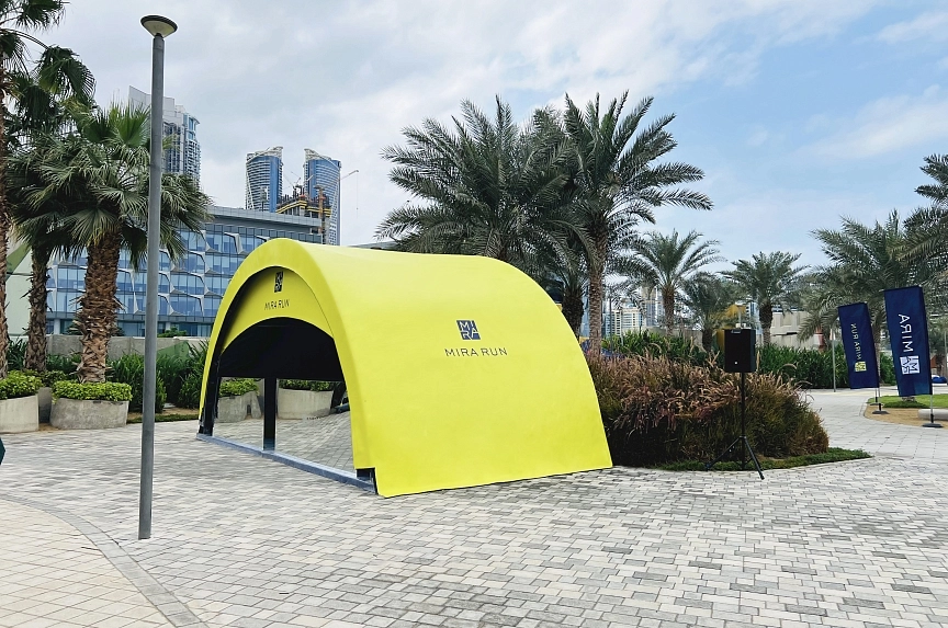 Bright yellow custom-branded Mira Run tent with blue interior entrance and high-visibility double-sided printing in Dubai urban plaza with skyscraper backdrop